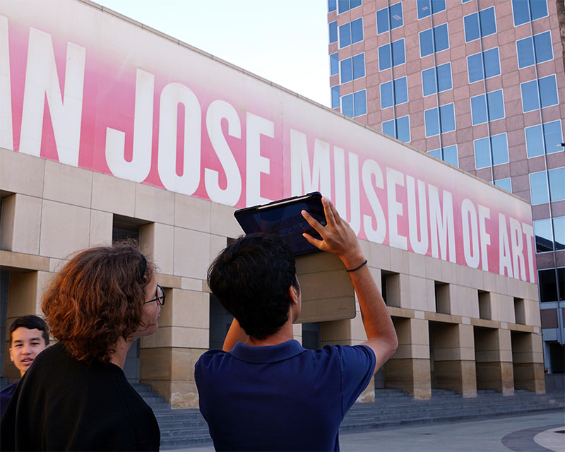 two students use a tablet to photograph a building facade with bold text